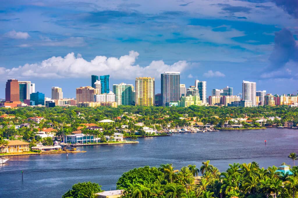 A view of a city skyline with high-rise buildings behind a wide river, palm trees, and residential neighborhoods highlights one of the most scenic urban locations under a partly cloudy sky.
