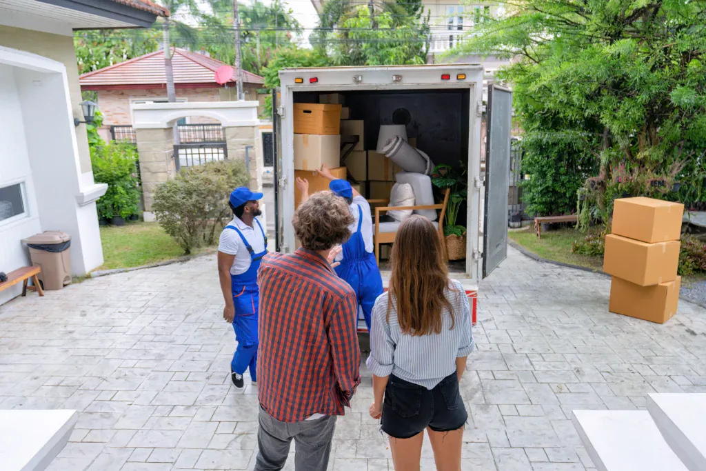 A couple watches a long distance moving truck as it prepares to transport their belongings.